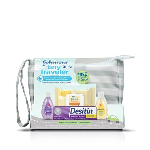 Una bolsa transparente contiene productos para el cuidado del bebé, como loción, jabón, champú y un envase morado, que descansa sobre una superficie blanca. Texto: "Set de regalo para bebé Johnson's Tiny Traveler".