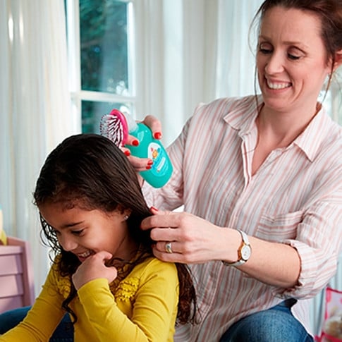 La madre usa el spray desenredante para bebé No More Tangles Johnson's Baby y peina el cabello mojado de su hija, ambas sonriendo en una habitación luminosa.