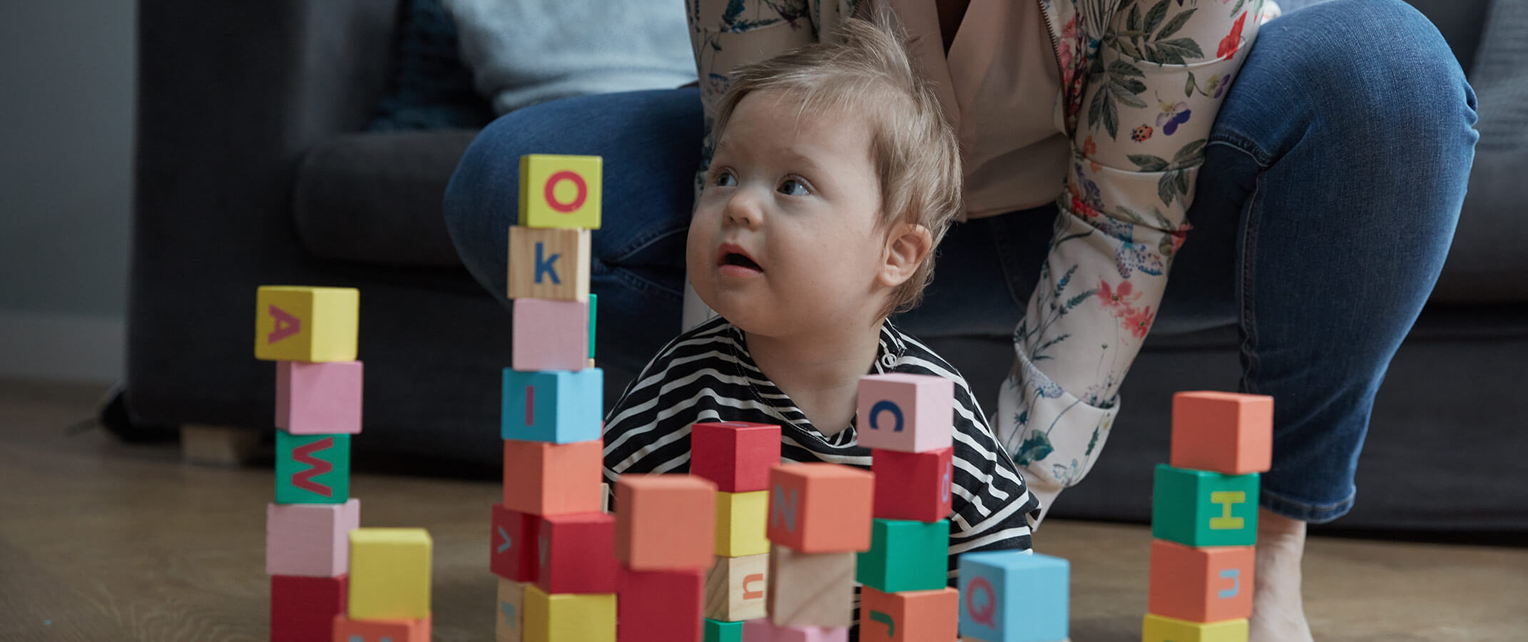 Un niño pequeño jugando con bloques de alfabeto de colores, con su madre ayudando en el fondo.