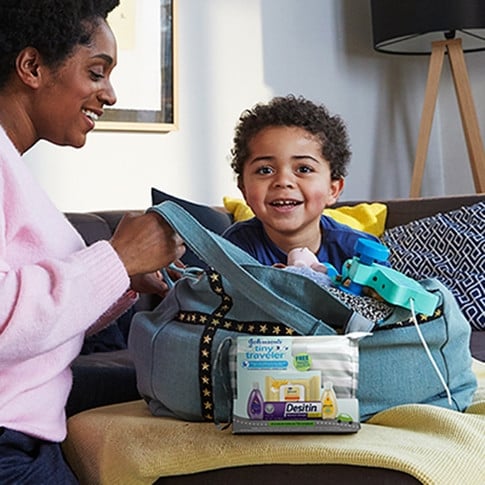 Madre e hijo empacando una bolsa con un set de regalo para bebé Johnson's Tiny Traveler, que incluye cuatro productos para bebé y un estuche para viaje gratis.