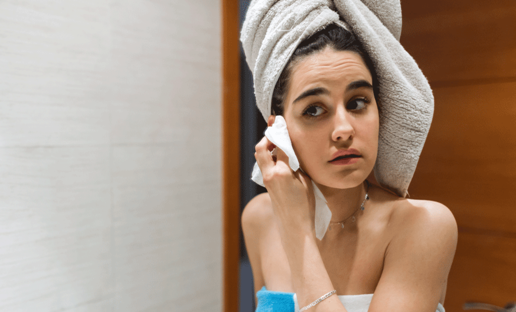Una joven con una toalla en la cabeza se limpia la cara después de salir de la ducha