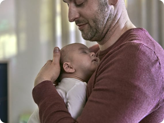 Papá que sostiene junto al pecho a su bebé recién nacido 